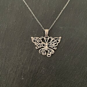 May include: A silver butterfly pendant necklace with a delicate, intricate design. The pendant is made of filigree and has a detailed body and wings.