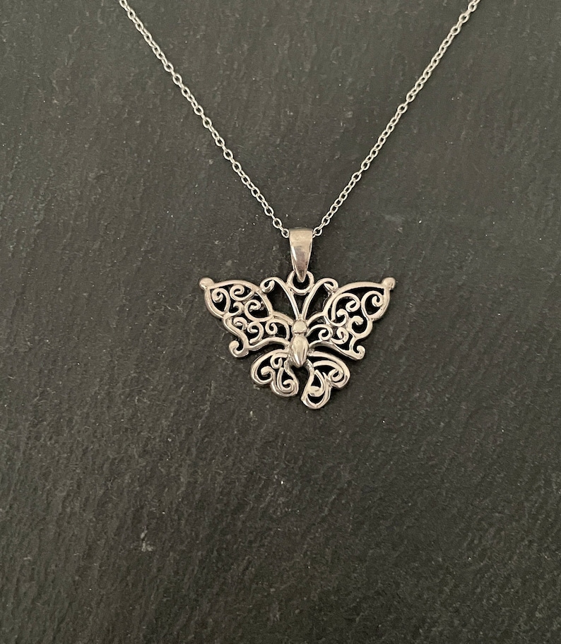 May include: A silver butterfly pendant necklace with a delicate, intricate design. The pendant is made of filigree and has a detailed body and wings.