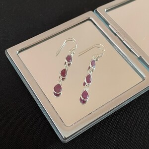 May include: A pair of silver dangle earrings with four teardrop-shaped red gemstones.