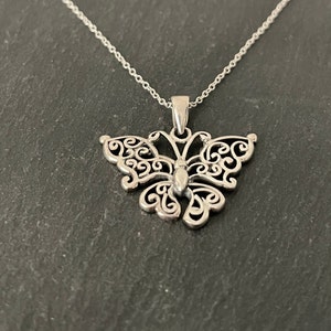 May include: A silver butterfly pendant necklace with a delicate filigree design. The pendant is attached to a silver chain.