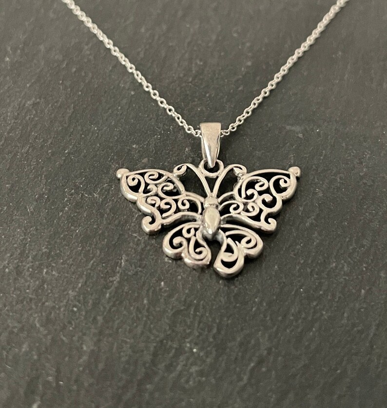 May include: A silver butterfly pendant necklace with a delicate filigree design. The pendant is attached to a silver chain.