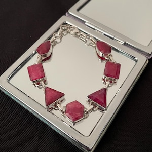 May include: A silver bracelet with pink gemstones. The bracelet has a chain link design and features a variety of gemstone shapes, including squares, triangles, and hexagons.