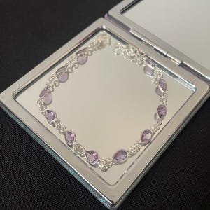 Könnte beinhalten: Ein silbernes Kettenarmband mit hellvioletten tropfenförmigen Edelsteinen.