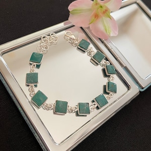 May include: A silver bracelet with square turquoise stones. The bracelet is on a silver background.