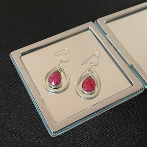 May include: A pair of silver dangle earrings with teardrop-shaped red gemstones.