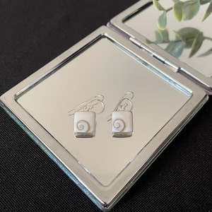 Pode incluir: Um par de brincos de prata com detalhes quadrados de concha branca com um design em espiral.