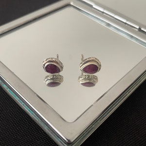 Pode incluir: Um par de brincos de prata com uma gema de rubi em forma de lágrima em cada brinco.