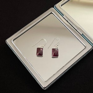 Puede incluir: Un par de pendientes de plata con piedras preciosas rojas cuadradas.