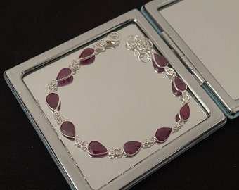 Puede incluir: Un brazalete de plata con un diseño de cadena y piedras preciosas de color púrpura en forma de lágrima.