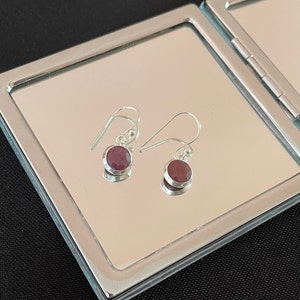 May include: A pair of silver dangle earrings with round, dark red gemstones.