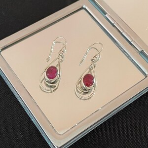 Peut inclure: Une paire de boucles d'oreilles pendantes en argent avec des accents de pierres précieuses roses. Les boucles d'oreilles présentent un design en forme de larme avec un fil d'argent délicat enroulé autour de la pierre précieuse.