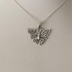 May include: A silver necklace with a delicate butterfly pendant. The butterfly is made of intricate filigree work and has a detailed body.
