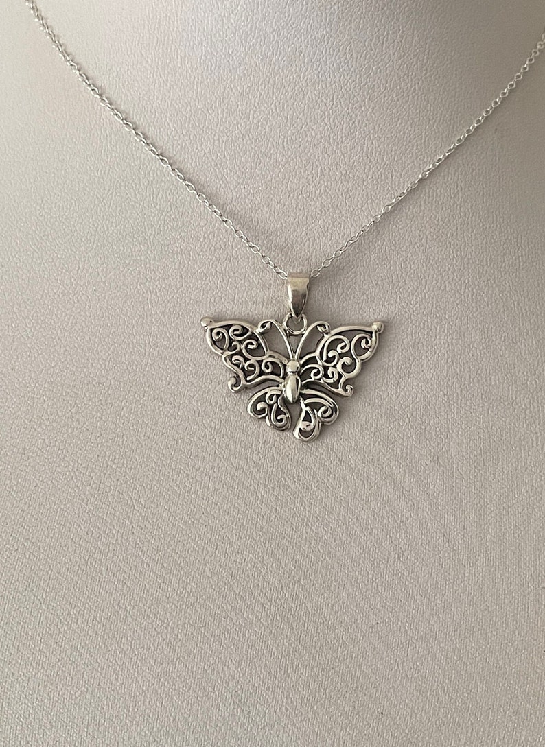 May include: A silver necklace with a delicate butterfly pendant. The butterfly is made of intricate filigree work and has a detailed body.