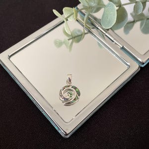 May include: A circular silver pendant featuring a swirling spiral design inlaid with iridescent abalone shell segments in shades of green, purple, and blue. The pendant includes a small silver bail at the top for attachment to a necklace chain.
