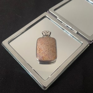 May include: A silver pendant with a rectangular, light brown stone with a swirling pattern. The stone is set in a silver frame with a decorative bail.