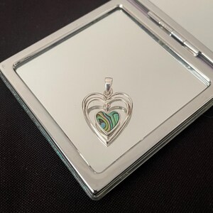May include: A silver heart pendant with a smaller abalone shell heart inside. The pendant has a layered, three-dimensional design.