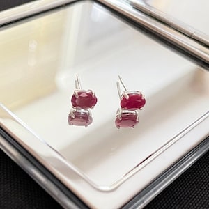 May include: A pair of silver stud earrings with oval-shaped red gemstones.