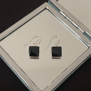 May include: A pair of silver earrings with black square-shaped stones. The earrings are hanging from a mirror.