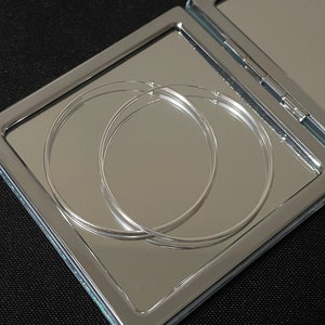 Puede incluir: Dos pendientes de aro plateados reflejados en un espejo compacto plateado.