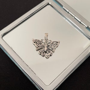 May include: A silver butterfly pendant with intricate filigree details. The pendant is displayed on a silver background.