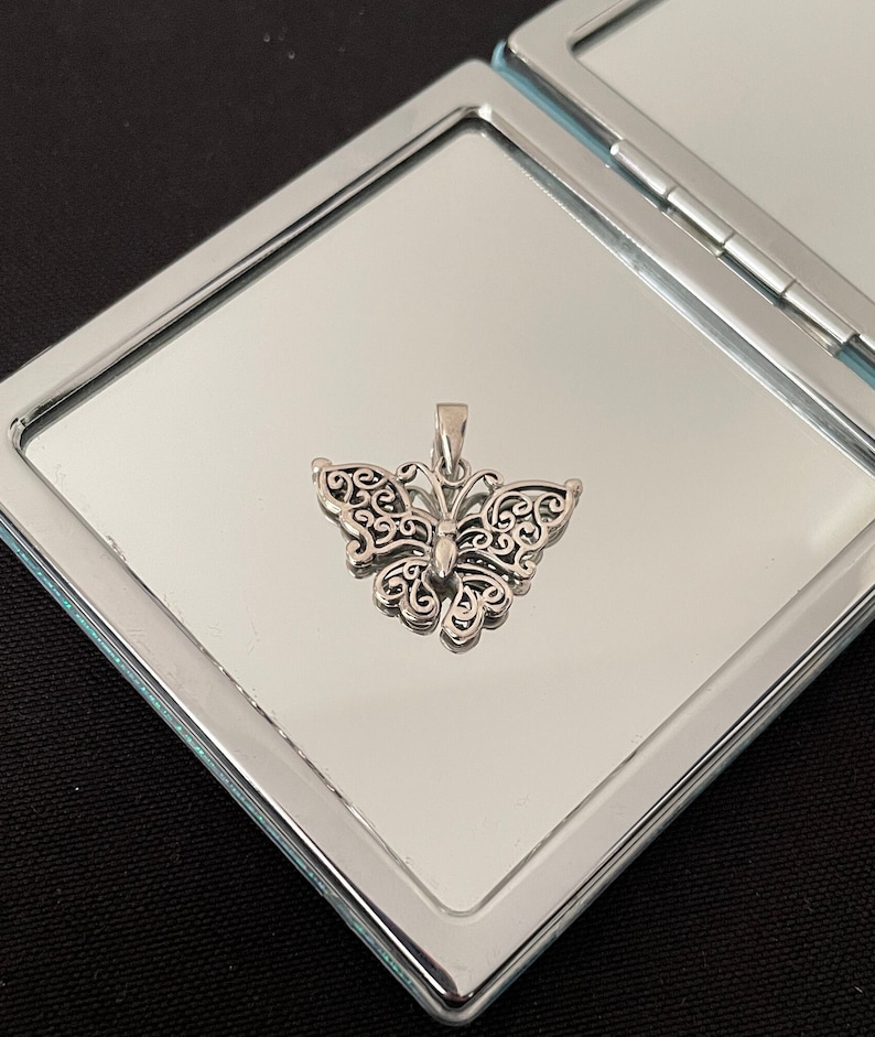 May include: A silver butterfly pendant with intricate filigree details. The pendant is displayed on a silver background.