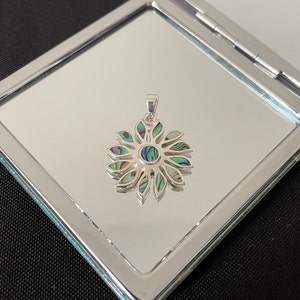 May include: A silver pendant featuring a flower design with iridescent abalone shell inlay. The flower has a central circle and multiple petals.