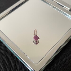Può includere: Un piccolo ciondolo d'argento con una pietra preziosa rotonda di colore rosa scuro.