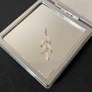 Può includere: Un ciondolo d'argento con un delicato design a ramo con cinque foglie madreperlacee bianche.