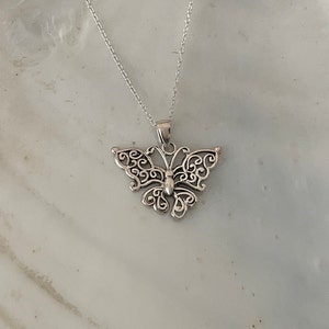 May include: A silver necklace with a delicate butterfly pendant. The butterfly is made of intricate filigree work and has a detailed body.
