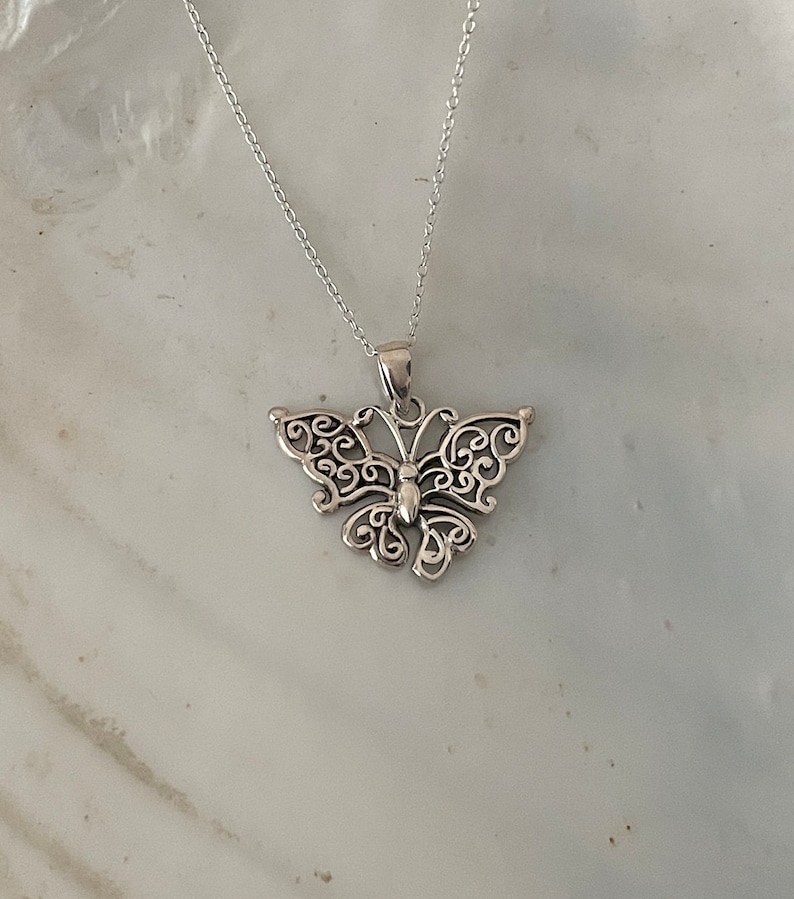 May include: A silver necklace with a delicate butterfly pendant. The butterfly is made of intricate filigree work and has a detailed body.