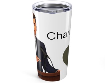 Puede incluir: Vaso térmico blanco con una ilustración de dibujos animados de una persona hablando en un podio. El vaso tiene una tapa negra y la palabra "Charl" está impresa en el lateral. La persona lleva un traje oscuro y corbata.