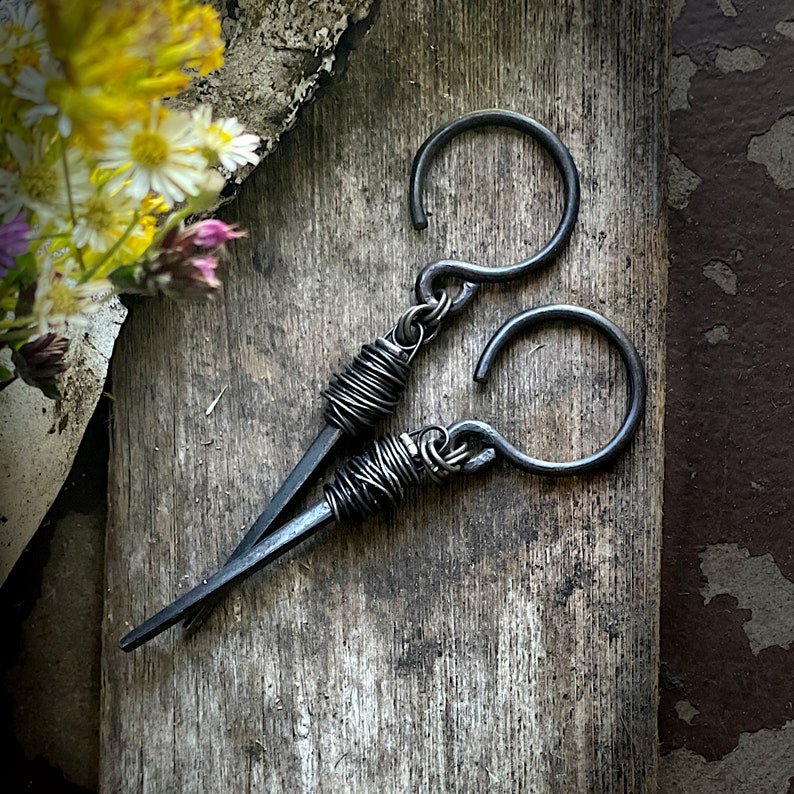 May include: A pair of black metal earrings with a unique wire-wrapped design. The earrings are made of thick gauge wire and have a simple hook closure.
