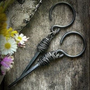 May include: A pair of black metal earrings with a wire wrapped design. The earrings are made of thick gauge wire and have a simple, modern look.