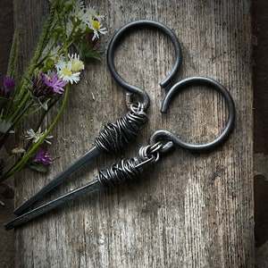 May include: A pair of black metal earrings with a unique twisted wire design. The earrings are made of thick gauge wire and have a rustic, industrial look.