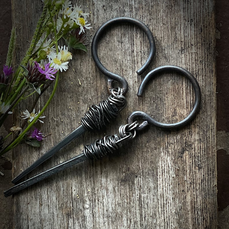 May include: A pair of black metal earrings with a unique twisted wire design. The earrings are made of thick gauge wire and have a rustic, industrial look.
