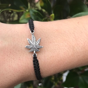 May include: Black braided bracelet with a silver marijuana leaf charm.