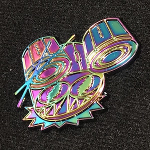 May include: A rainbow iridescent enamel pin featuring a cartoon drum set with a stylized face. The drums are outlined in gold and have a black background.