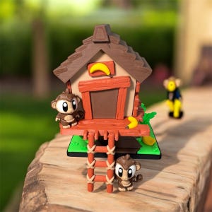 Puede incluir: Un juego temático de monos que presenta una casa en el árbol con un techo marrón, una puerta roja y un plátano amarillo. Dos monos están posados en la estructura, y una escalera conduce a la base. Un tercer mono está en el fondo.