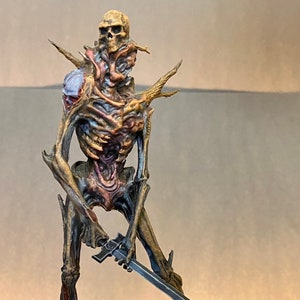 May include: A skeletal figure with a skull head and a sword, painted in a variety of colors, including gold, blue, and red. The figure is standing on a rocky base.