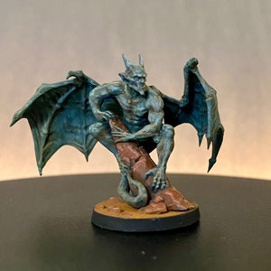 May include: A blue and green gargoyle figurine with wings perched on a rock. The gargoyle has a menacing expression and sharp claws.