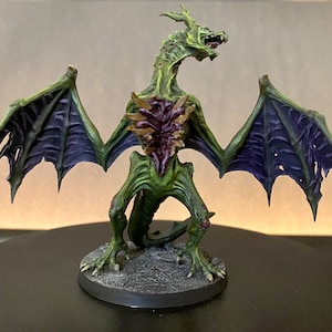 May include: A green and purple painted miniature dragon with wings spread wide. The dragon has a ripped open chest revealing a fleshy, purple, and brown interior.