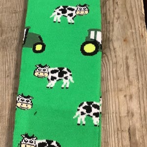 May include: Green socks with a pattern of black and white cows and green tractors. The socks have the text "Oates Welly Socks" on the tag.