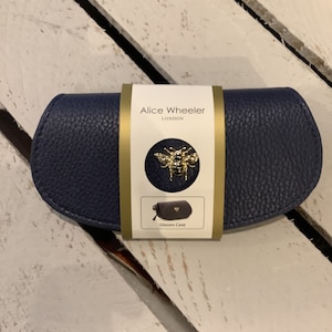 May include: A navy blue glasses case with a gold bee design and the text "Alice Wheeler LONDON" on the front. The case is made of a textured material and has a gold zipper.