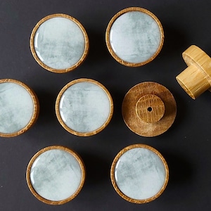 May include: A collection of wooden cabinet knobs with a light blue and white circular design. The knobs have a gold-colored border and are arranged on a dark surface. One knob is detached, showing the wooden stem.