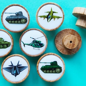 May include: Six wooden knobs featuring various military vehicle designs. The knobs are round and have a white background with a colourful image of a tank, helicopter, or aeroplane. The knobs are ideal for adding a touch of whimsy to any room.