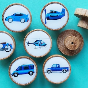 May include: Set of seven wooden knobs with blue and white illustrations of various vehicles, including a car, a helicopter, a plane, a truck, a van, a scooter, and a plain knob.