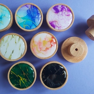 Può includere: Otto pomelli rotondi in legno con intarsi in resina di diversi colori. Gli intarsi in resina presentano motivi astratti in tonalità di blu, rosa, bianco, verde e nero.