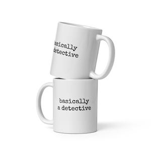 May include: Two white ceramic mugs, one stacked on top of the other. The bottom mug displays the text "basically a detective" in black. The top mug shows the same text, partially visible. Both mugs have a curved handle.