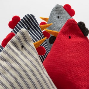 May include: Three plush toy chickens in different colors and patterns. The first chicken is white with blue stripes, the second is blue with white stripes, and the third is red. Each chicken has a yellow beak and a red comb.