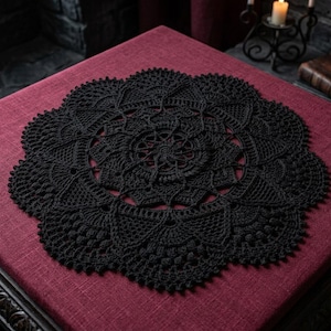 Könnte beinhalten: Eine kreisförmige, schwarze Häkeldeckchen mit einem komplizierten, symmetrischen, von Mandalas inspirierten Muster mit strahlenförmigen Stichen, gewellten Rändern und durchbrochenen Details, die eine dichte, texturierte Fadenkonstruktion aufweist.